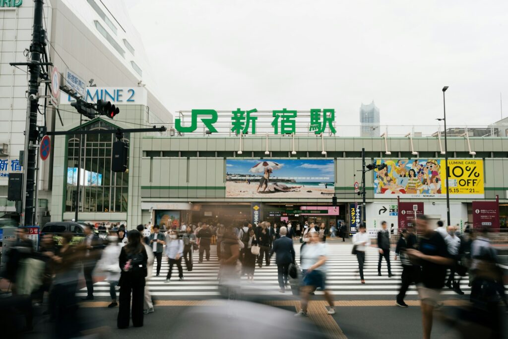 People cross a busy street in front of a train station.